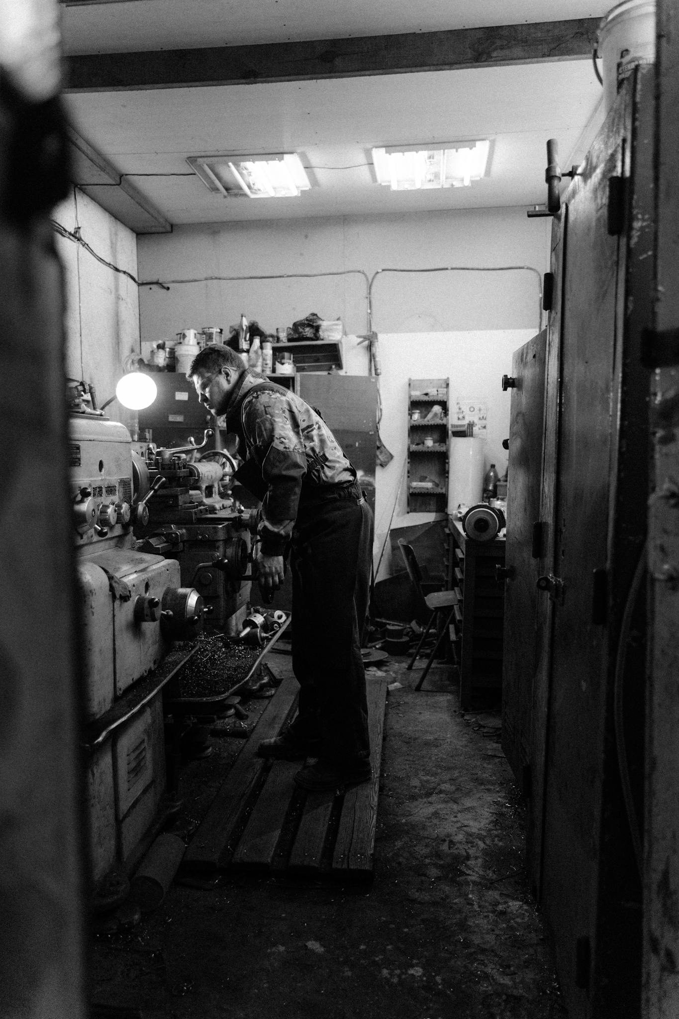 Black and white image of a man working on a lathe machine in an industrial workshop.
